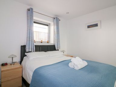 A bedroom with a bed covered in white sheets and a blue blanket with rolled towels on top at 28 Zenith in Porth