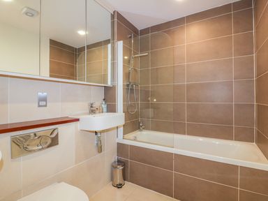 A bathroom with a bathtub shower combination a wall-mounted sink a mirrored cabinet and a toilet at 28 Zenith in Porth