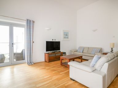 A living room with two sofas a wooden coffee table a TV on a wooden stand and glass doors with curtains at 28 Zenith in Porth