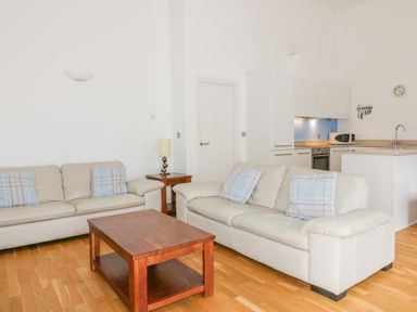 A living room with two white sofas and a wooden coffee table near a kitchen at 28 Zenith in Porth