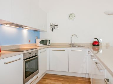 A kitchen with white cabinets oven microwave wall clock knife rack and a red kettle at 28 Zenith in Porth