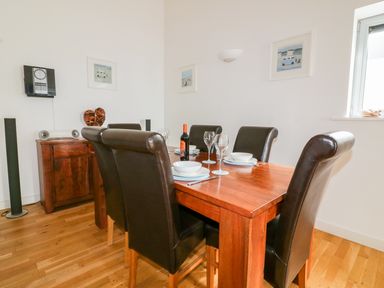 A dining room with a wooden table set with bowls glasses and a bottle of wine surrounded by six leather chairs at 28 Zenith in Porth