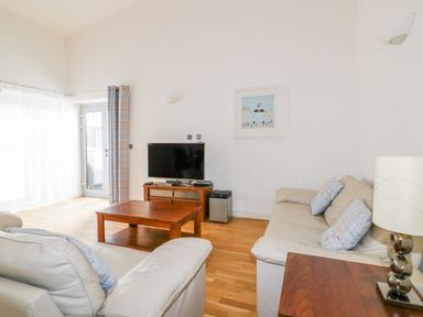 A living room with two cream sofas a wooden coffee table a TV on a wooden stand and a lamp on a wooden side table at 28 Zenith in Porth
