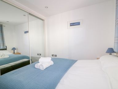 A bedroom with a bed covered by a blue blanket and white towels on top with mirrored closet doors at 28 Zenith in Porth