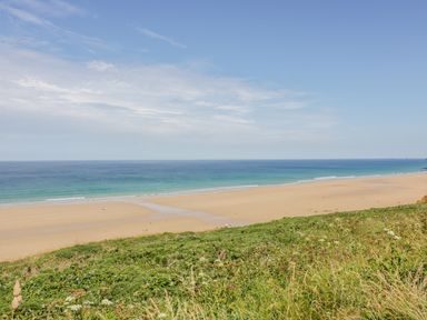 A sandy beach with scattered people and ocean waves viewed from a grassy hill at 28 Zenith in Porth