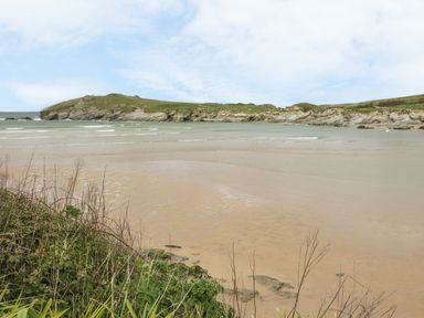 A sandy beach with shallow water and rocky cliffs in the background at 28 Zenith in Porth