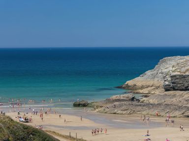 A beach with people walking and swimming near the water
