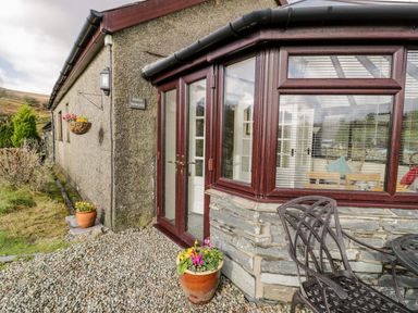 Exterior view of a stone and pebble covered house entrance with a potted plant and metal outdoor furniture at Melin Newydd in Porthmadog