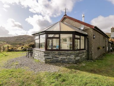 Exterior view of a house with a conservatory and a small table with two chairs outside on a gravel area at Melin Newydd in Porthmadog