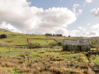 A rural landscape with a stone building a wooden gate and grassy fields at Melin Newydd in Porthmadog