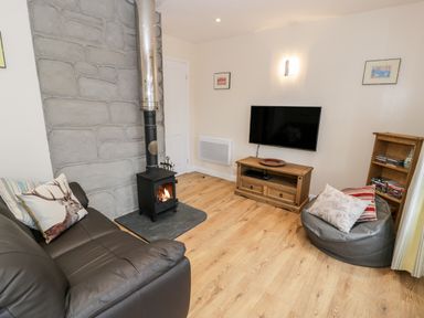 A living room with a leather sofa a wood burning stove a wall mounted tv a wooden cabinet and a bean bag chair at Melin Newydd in Porthmadog