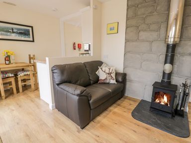 A living room with a leather sofa a wood burning stove and a dining table with chairs at Melin Newydd in Porthmadog