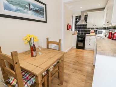 A kitchen with wooden floor a wooden dining table with two chairs a bottle with two glasses and yellow flowers on the table a stove a microwave a kettle and a toaster at Melin Newydd in Porthmadog
