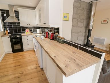 A kitchen with white cabinets black tiles wooden countertop and appliances at Melin Newydd in Porthmadog
