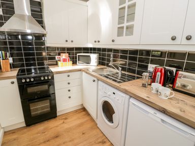 A kitchen with white cabinets black tiled backsplash wooden countertops and appliances at Melin Newydd in Porthmadog
