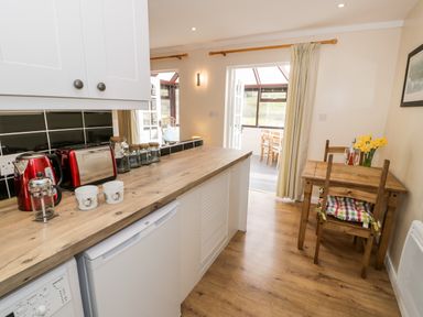 A kitchen with wooden countertop appliances and a small dining table with chairs and flowers at Melin Newydd in Porthmadog