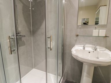 A bathroom with a glass enclosed shower and a white pedestal sink with a mirror above at Melin Newydd in Porthmadog