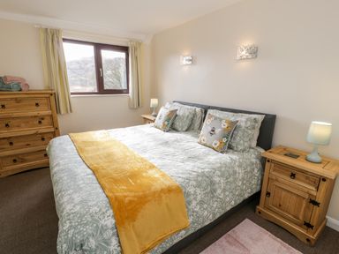 A bedroom with a bed with patterned bedding and yellow throw a wooden chest of drawers bedside tables with lamps and folded towels on the chest of drawers at Melin Newydd in Porthmadog