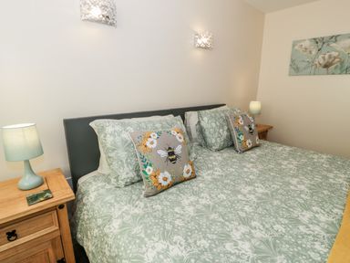 A bedroom with a double bed green and white bedding bee patterned cushions bedside tables and lamps at Melin Newydd in Porthmadog