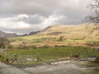 A rural landscape with green fields fenced by metal gates and hills in the background at Melin Newydd in Porthmadog