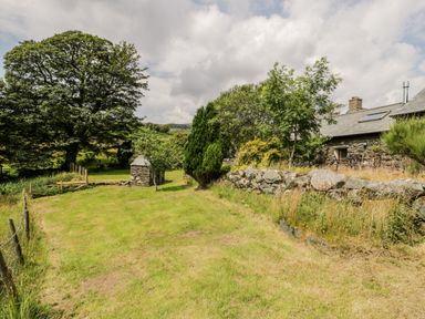 A garden area with grass trees and a stone wall next to a stone house at Melin Newydd in Porthmadog