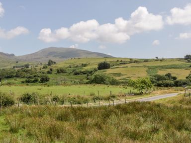 A rural landscape with rolling green hills a gravel road and scattered trees at Melin Newydd in Porthmadog