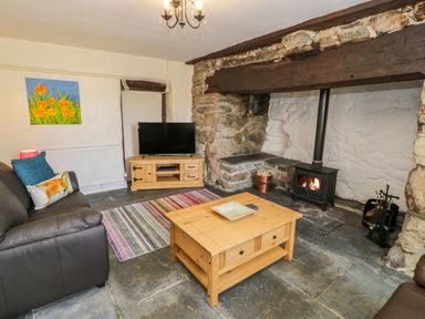 A living room with a brown sofa a wooden coffee table a television on a wooden stand and a wood-burning stove at Bwthyn Pennant in Porthmadog