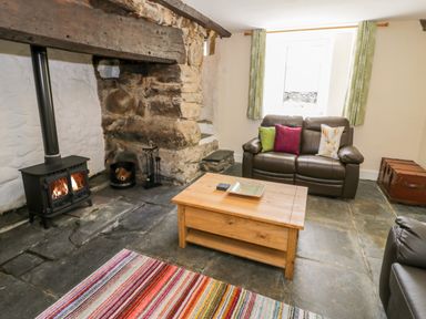 A living room with a wood burning stove a brown leather sofa with cushions a wooden coffee table and a striped rug at Bwthyn Pennant in Porthmadog