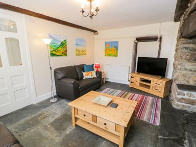 A living room with a sofa a television on a wooden stand a wooden coffee table and colorful paintings on the walls at Bwthyn Pennant in Porthmadog