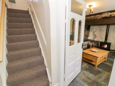 A staircase with carpet leading up beside a door opening to a room with a wooden coffee table and a wood burning stove at Bwthyn Pennant in Porthmadog