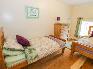 A bedroom with two single wooden beds a wooden dresser and a window with green curtains at Bwthyn Pennant in Porthmadog