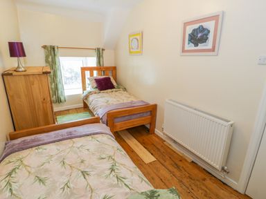 A bedroom with two single wooden beds a wooden chest of drawers a lamp and green curtains at Bwthyn Pennant in Porthmadog