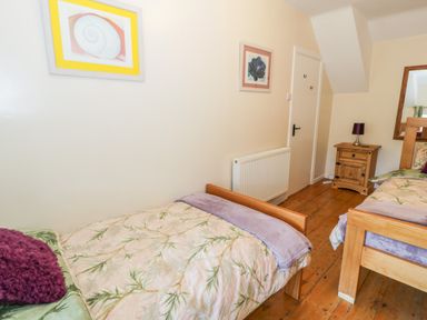 A bedroom with two single wooden beds a wooden nightstand with a lamp a wall radiator and framed pictures at Bwthyn Pennant in Porthmadog