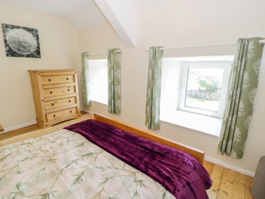 A bedroom with a wooden dresser bed with a floral bedspread and green curtains at Bwthyn Pennant in Porthmadog