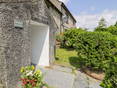 Exterior entrance to a stone house with a garden path and green bushes at Bwthyn Pennant in Porthmadog
