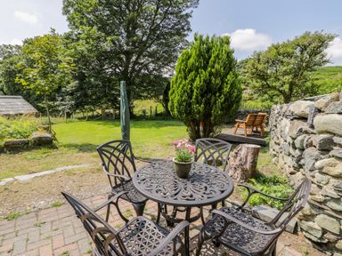 A garden patio with a round metal table and four chairs and a potted plant on the table at Bwthyn Pennant in Porthmadog