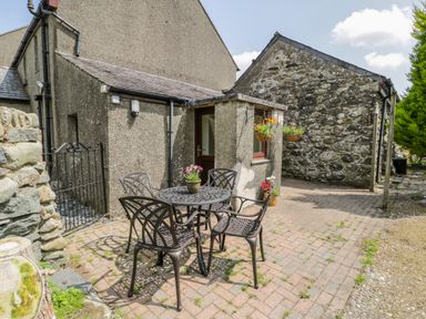 A patio with a round metal table and four metal chairs outside a stone and stucco house at Bwthyn Pennant in Porthmadog