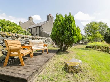An outdoor area with wooden benches on a wooden deck near stone walls and trees at Bwthyn Pennant in Porthmadog