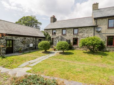 A stone house with a slate roof and a garden with shrubs and a stone path at Bwthyn Pennant in Porthmadog