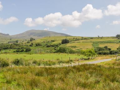 A grassy rural landscape with a road running through it and hills in the background at Bwthyn Pennant in Porthmadog