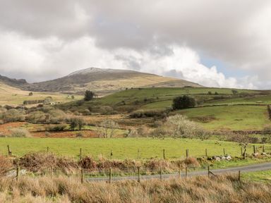 A rural landscape with green fields trees and a distant hill under a cloudy sky at Bwthyn Pennant in Porthmadog