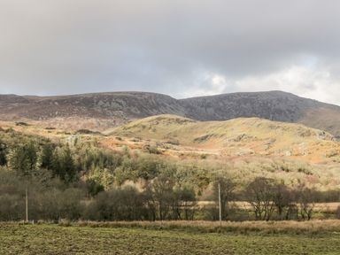A landscape of hills with trees and grass under a partly cloudy sky at Bwthyn Pennant in Porthmadog
