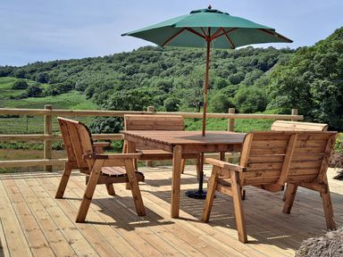 Wooden outdoor table with umbrella and chairs on a deck overlooking green hills at Bwthyn Pennant in Porthmadog