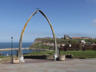 A large whale bone arch near benches overlooking a coastal town and the sea at Premier, Transit & Lady Hilda @ Engine Shed in Whitby