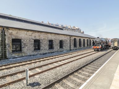 A stone building beside train tracks with a steam locomotive and train car at Premier Transit & Lady Hilda  Engine Shed in Whitby