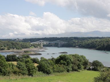 A river with a suspension bridge and trees on both sides at Ael Y Bryn in Menai Bridge