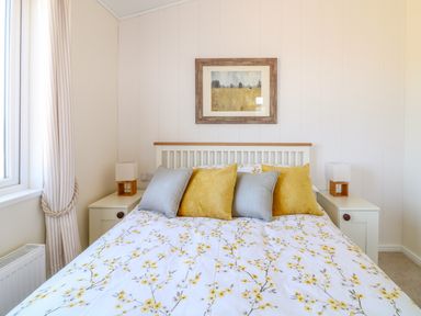 A bedroom with a bed with floral bedding yellow and gray pillows bedside tables with lamps and a framed picture on the wall at Ash Lodge in Teigngrace near Newton Abbot
