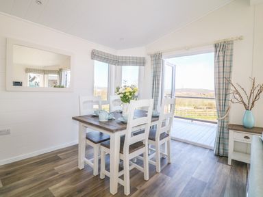 A dining area with a table and chairs set near windows and an open door at Ash Lodge in Teigngrace near Newton Abbot