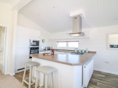 A kitchen with an island countertop with two stools and built in oven at Ash Lodge in Teigngrace near Newton Abbot