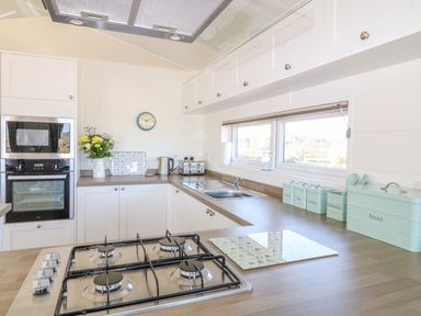 A kitchen with white cabinets a gas stove oven microwave and containers labeled sugar tea coffee utensils and bread at Ash Lodge in Teigngrace near Newton Abbot